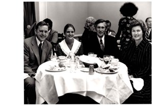 ["The image depicts Dewey Bartlett seated at a dinner table with Gretchen Moores, Ken Moores, and Ann Bartlett"]
